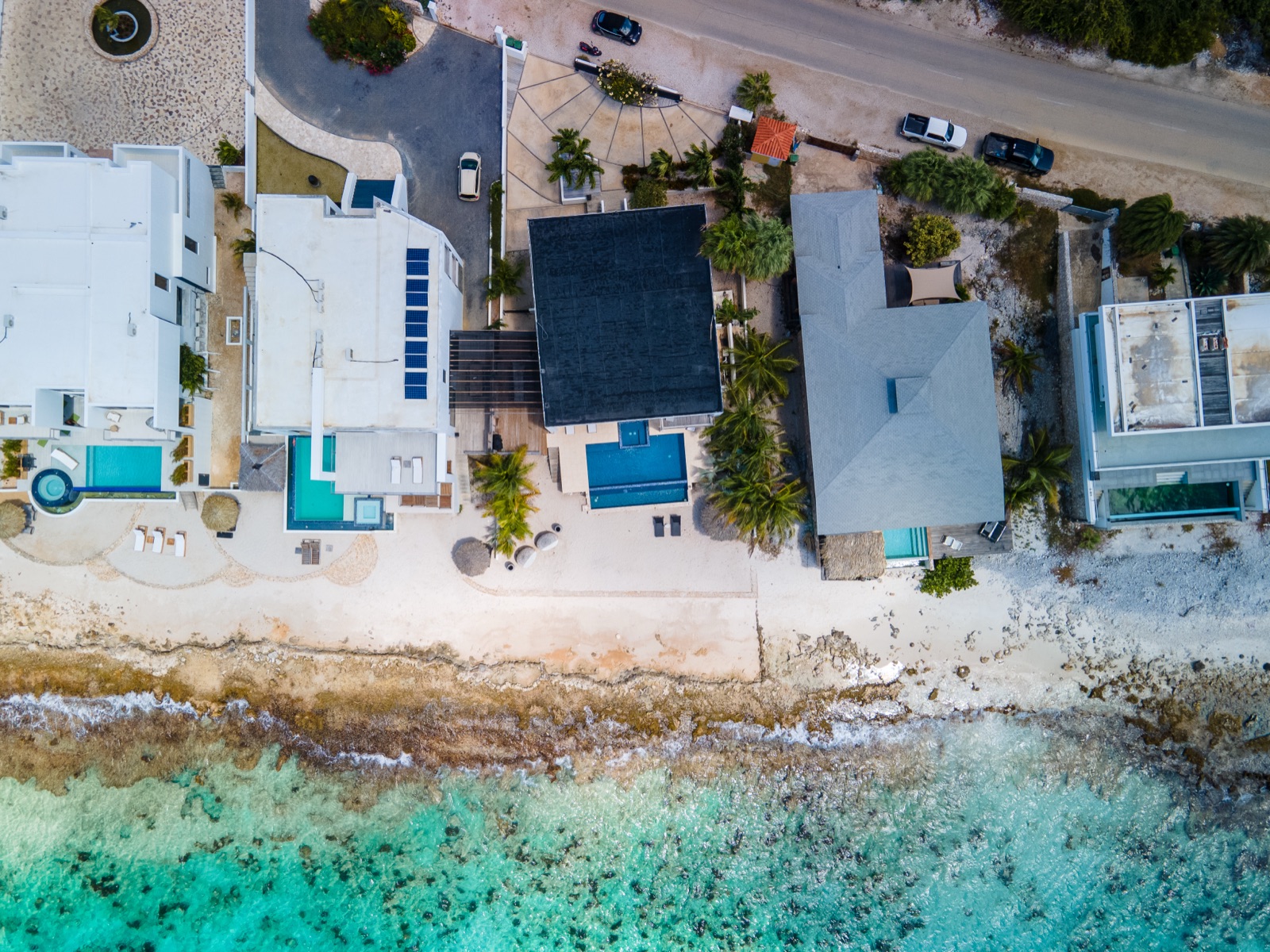 Aerial drone view of luxury Bonaire beachfront villas with private pools, white sand beach, and direct access to the turquoise Caribbean Sea.